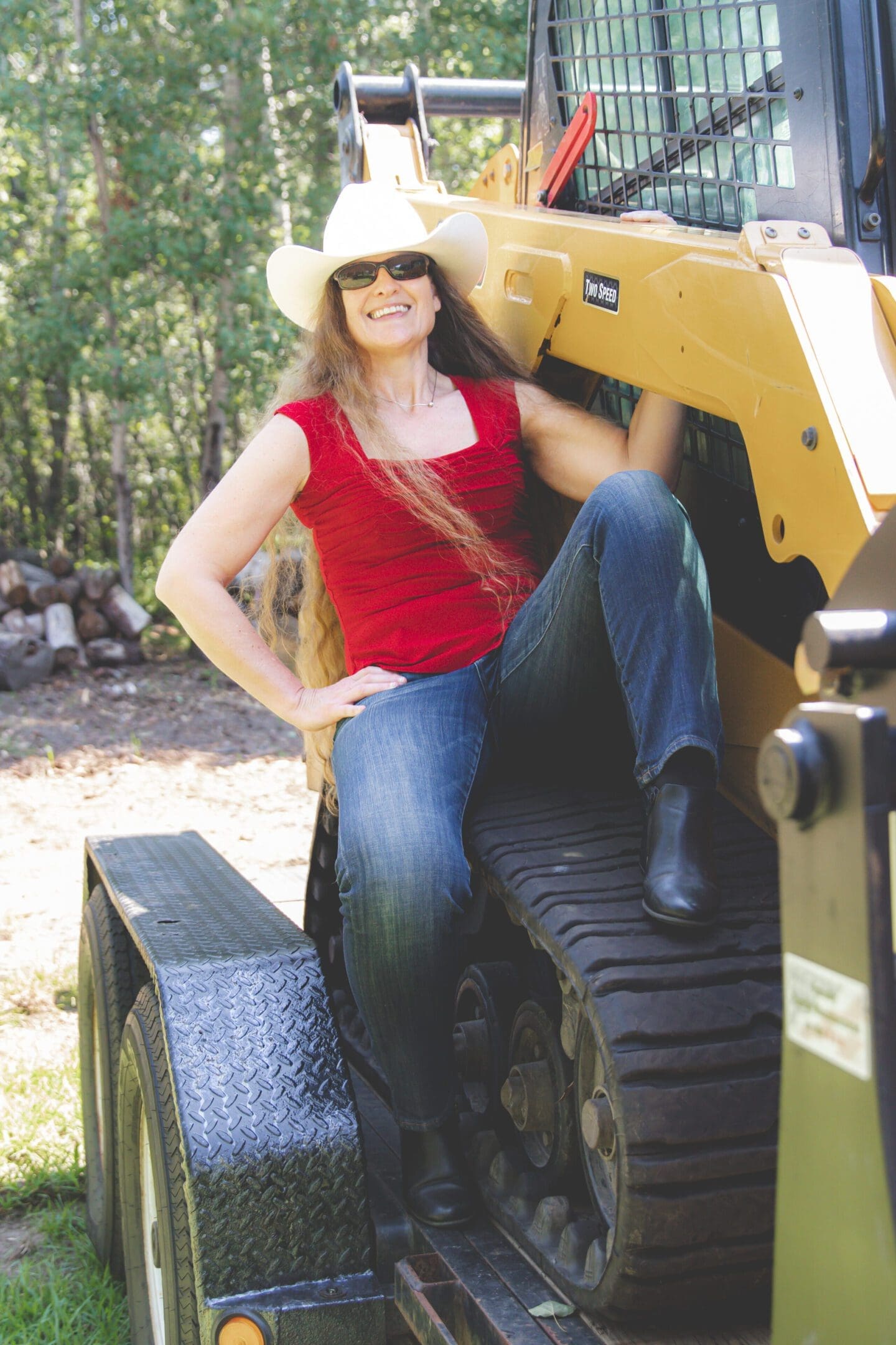 Woman in a cowboy hat posing on construction equipment outdoors.