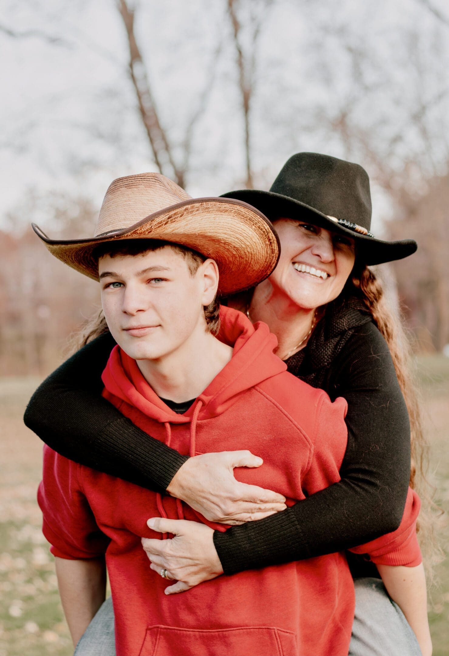 A young man and woman wearing cowboy hats, smiling outdoors.
